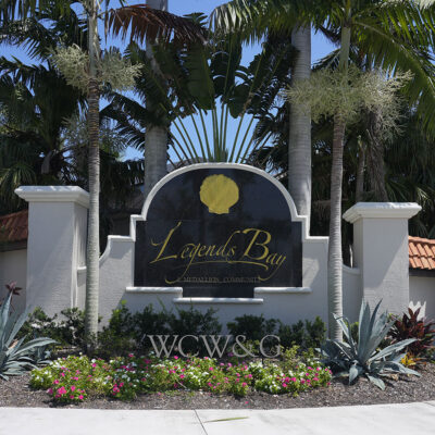 Entrance sign for Legends Bay Medallion Community, surrounded by palm trees, flowers, and tropical plants.
