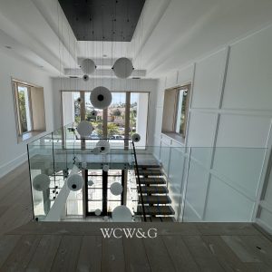 Modern staircase with glass railing, wooden steps, and spherical pendant lights in a bright, white interior.