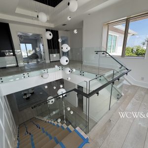 Modern staircase with glass railings, hanging orb lights, large window, and wood floors in a bright interior.