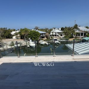 View from balcony overlooking a marina with docked boats, houses, palm trees, and clear blue sky in the background.
