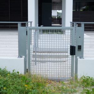 A metal security gate with a keypad lock stands in front of a modern white building with steps.