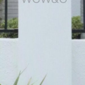 White rectangular pillar with rounded top, black fence behind, green plants at base, text “WCW&G” on pillar.