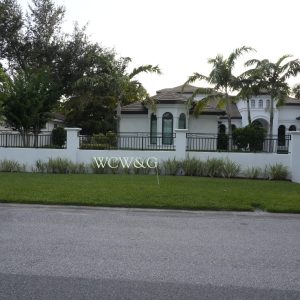 Large white house with a manicured lawn, palm trees, and “WCW&G” letters displayed in the front yard.