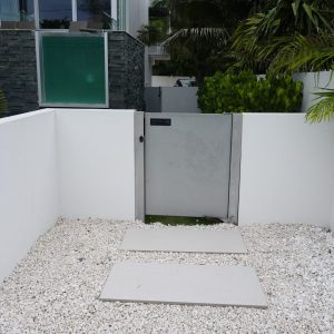 A modern metal gate set in a white wall, with a gravel path and rectangular stepping stones leading up to it.