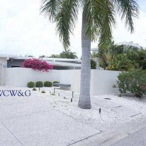 Modern house with white exterior, palm trees, and pink bougainvillea in the front yard, seen from the street.
