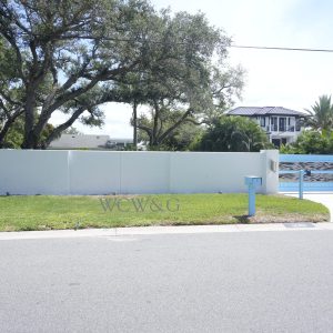 A modern house with a white wall, blue gate, and a well-kept lawn, viewed from across the street.