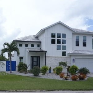 Modern two-story white house with large windows, attached garage, and landscaped front yard with palm trees and shrubs.