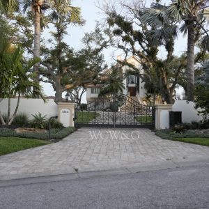 Gated entrance to a two-story house with palm trees and landscaped yard, viewed from the street.