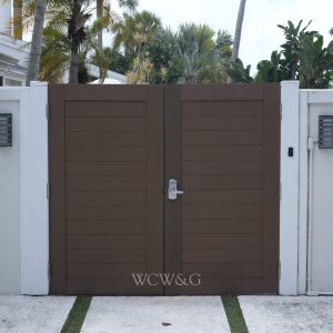 Brown double wooden gate with a silver handle, set in a white wall with outdoor lights on both sides.