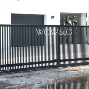 Black metal gate with vertical bars and “WGW&G” letters in front of a modern building with three garage doors.