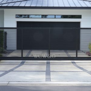 Modern black metal sliding gate in front of a white house with garage and landscaped entrance.