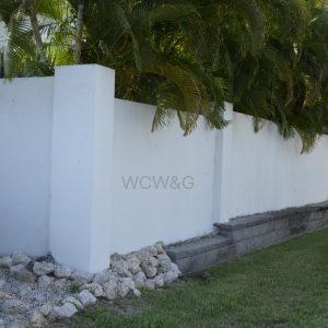 White concrete wall with green plants behind it, stone border at the base, and grass lawn in the foreground.