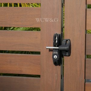 Wooden gate with horizontal slats, secured with a black metal latch and key lock; plants visible in the background.
