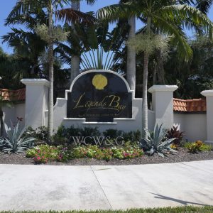 Entrance sign for Legends Bay community, surrounded by tropical plants and palm trees under a clear sky.